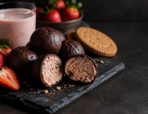 Energy balls με επικάλυψη σοκολάτας, κομμένες στη μέση, με φράουλες και ποτήρι κεφίρ φράουλα
